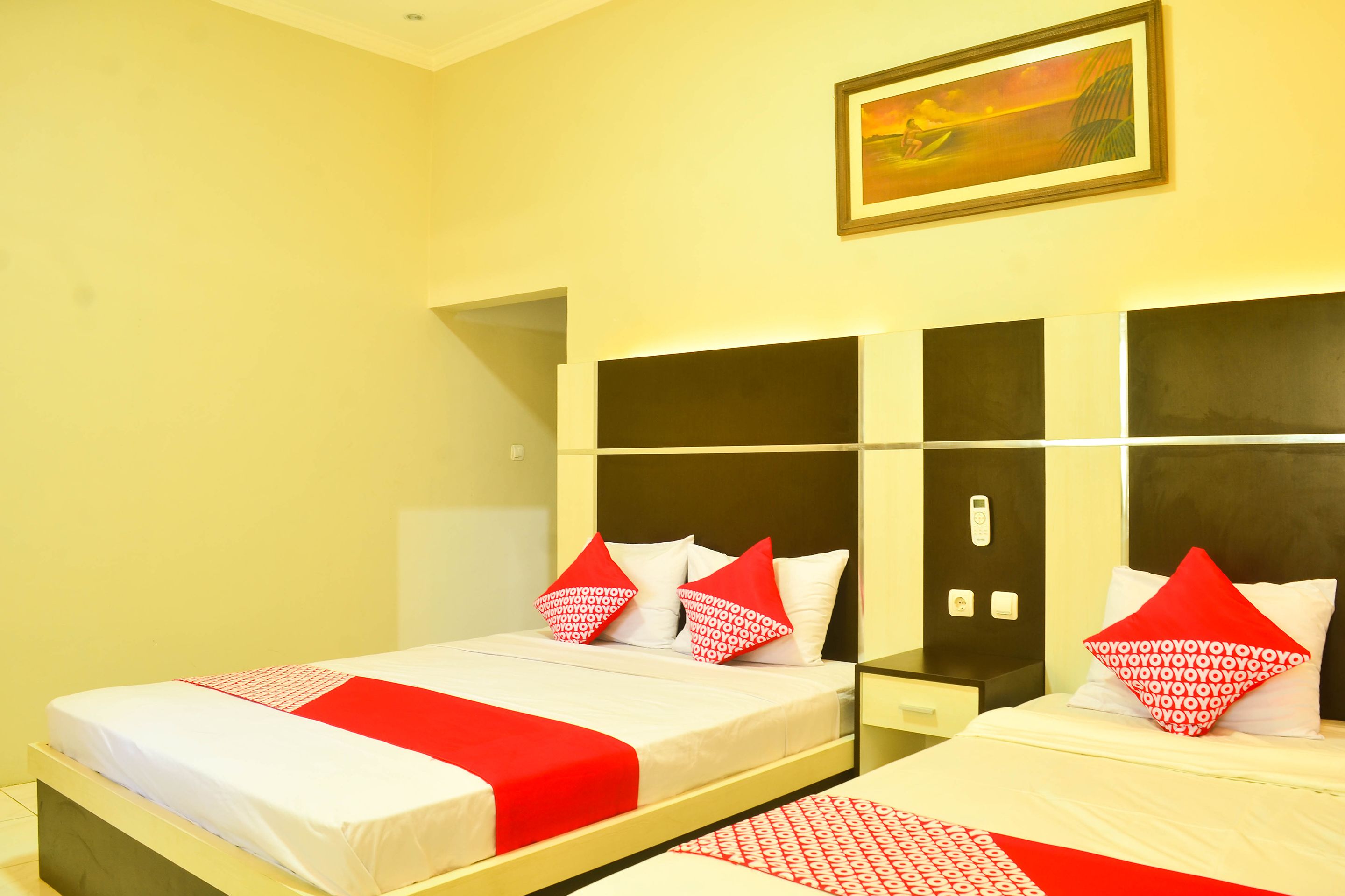 Habitación de hotel con dos camas, cada una con ropa de cama roja y blanca, un cuadro en la pared y una mesita entre las camas.