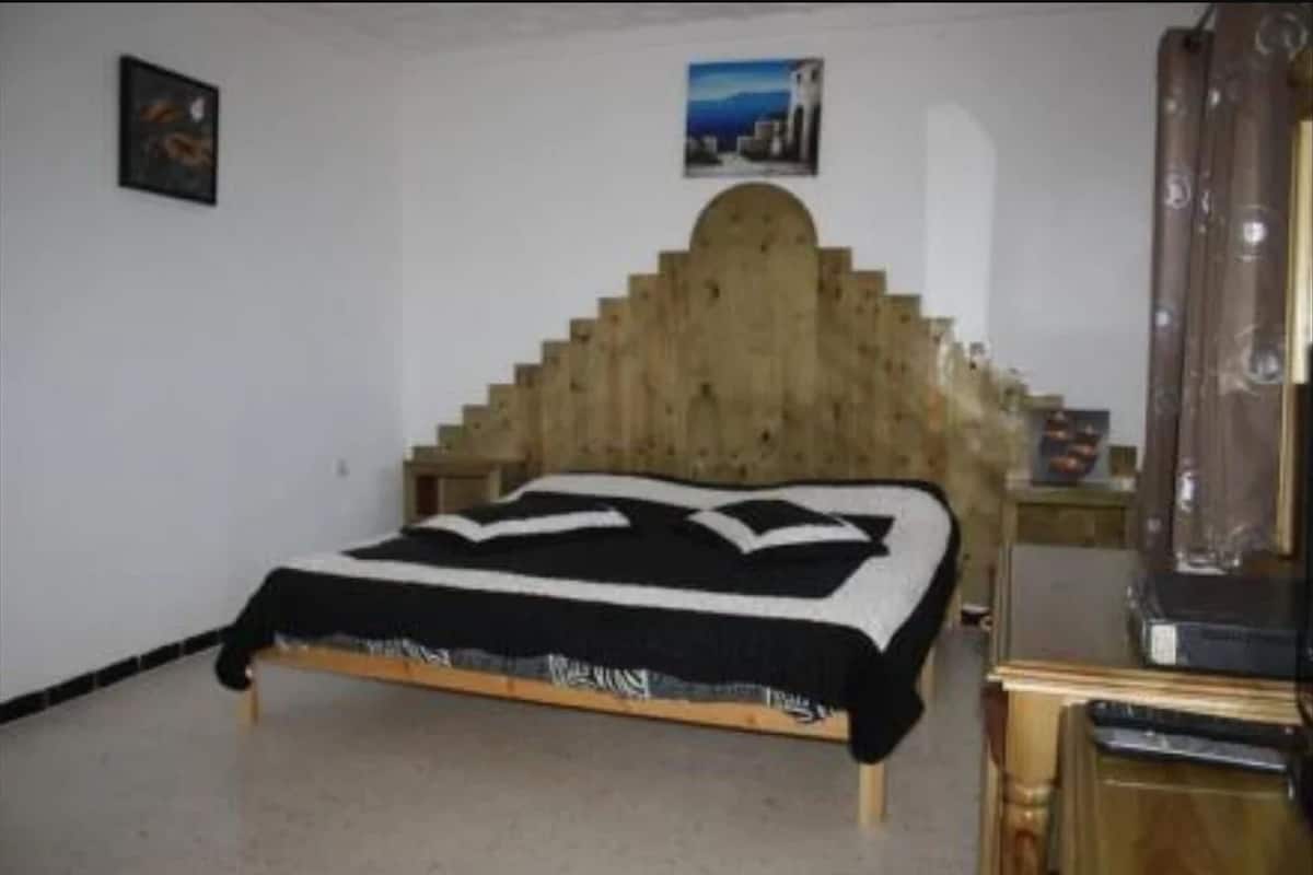 Ein Schlafzimmer mit einem hölzernen Kopfteil, einem Bett mit einer schwarz-weißen Tagesdecke und einem kleinen Tisch mit einer Lampe.