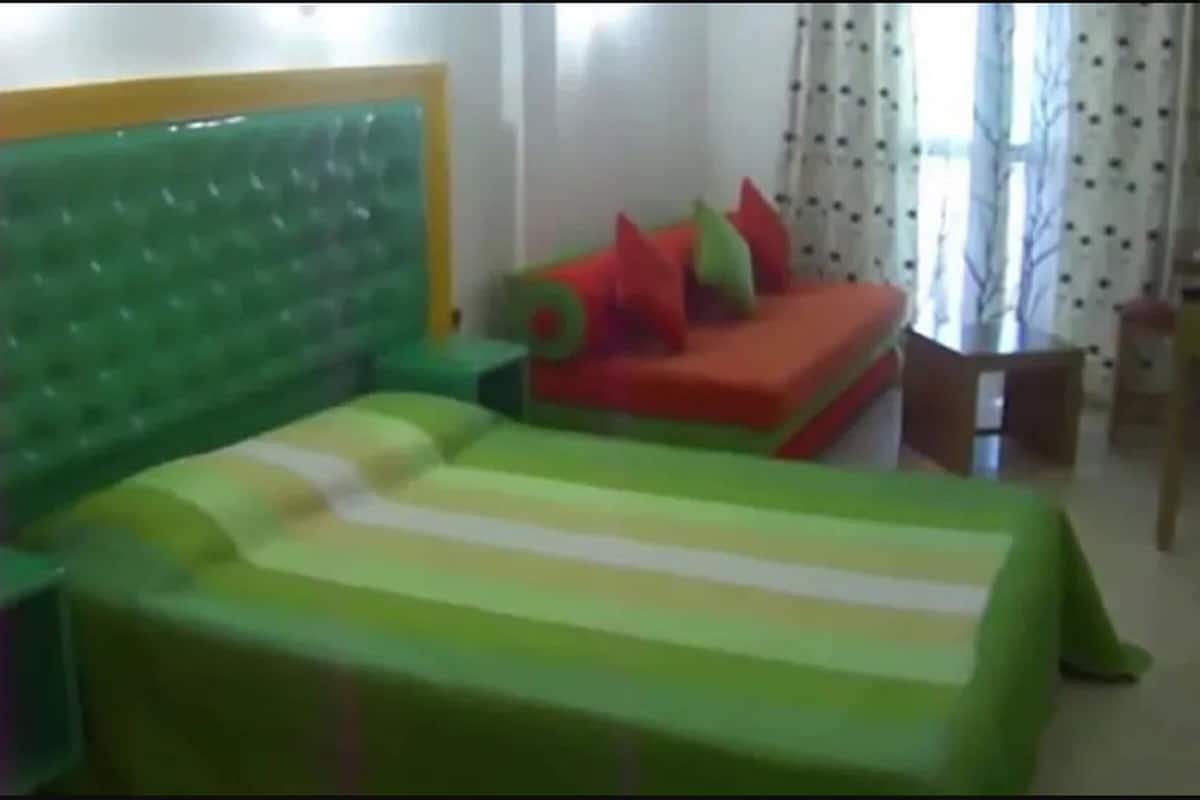 Ein Zimmer mit einem grünen gepolsterten Kopfteil, einem Bett mit gestreifter Bettdecke, einem rot-grünen Sofa und einem kleinen Tisch mit Stuhl.