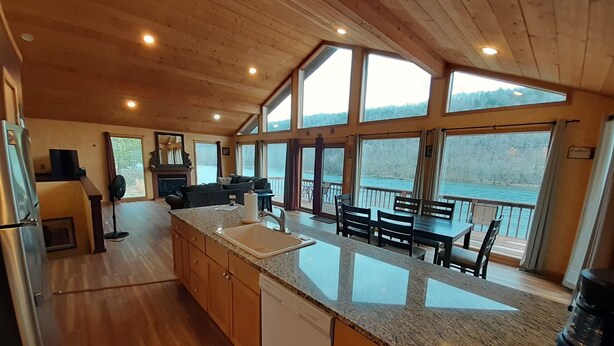 Eine geräumige Küche mit Granit Arbeitsplatten, Holzschränken und einem Geschirrspüler. Große Fenster bieten Blick auf einen See und einen Wald.