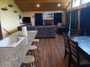 Una cocina con encimera de granito, taburetes de madera, un lavabo y una zona de comedor con mesa y sillas.