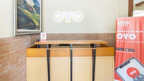 A reception desk with a framed painting above it, a sign for OYO Hotels, and a promotional poster for the OYO app. - Super OYO 890 Dewi Fortuna Guest House (Depok)