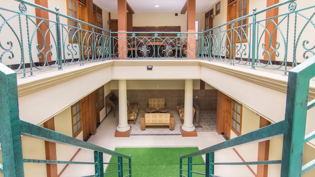 A multi-level hotel interior with a central staircase, a balcony with ornate railings, and a seating area with sofas and a coffee table. - Super OYO 890 Dewi Fortuna Guest House (Depok)