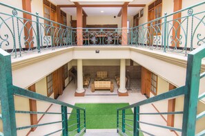 A multi-level hotel interior with a central staircase, a balcony with ornate railings, and a seating area with sofas and a coffee table. - Super OYO 890 Dewi Fortuna Guest House (Depok)