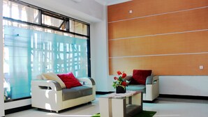 A modern living room with two sofas, a coffee table, and a large window with blinds. - OYO 783 Grand Mentari Guest House (Bengkulu)