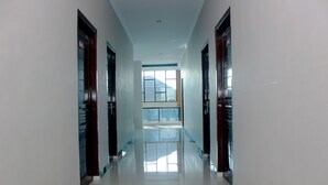 A long, narrow hallway with glossy white floors and dark wooden doors on both sides. A large window at the end allows natural light to enter. - OYO 783 Grand Mentari Guest House (Bengkulu)