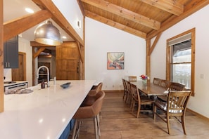 A spacious kitchen with a large island, wooden beams, and a dining area with a table and chairs.