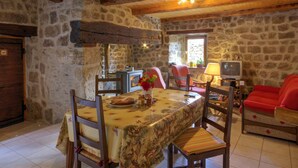 Un intérieur rustique avec des murs en pierre, un plafond en bois, une table à manger avec des chaises, un canapé et un téléviseur.