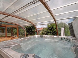 Un bain à remous doté d’une enceinte en verre, entouré d’une terrasse en bois et offrant une vue sur une maison et des arbres.