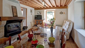 Una sala de estar acogedora con chimenea, vigas de madera en el techo, una mesa de comedor con sillas, un sofá y un televisor.