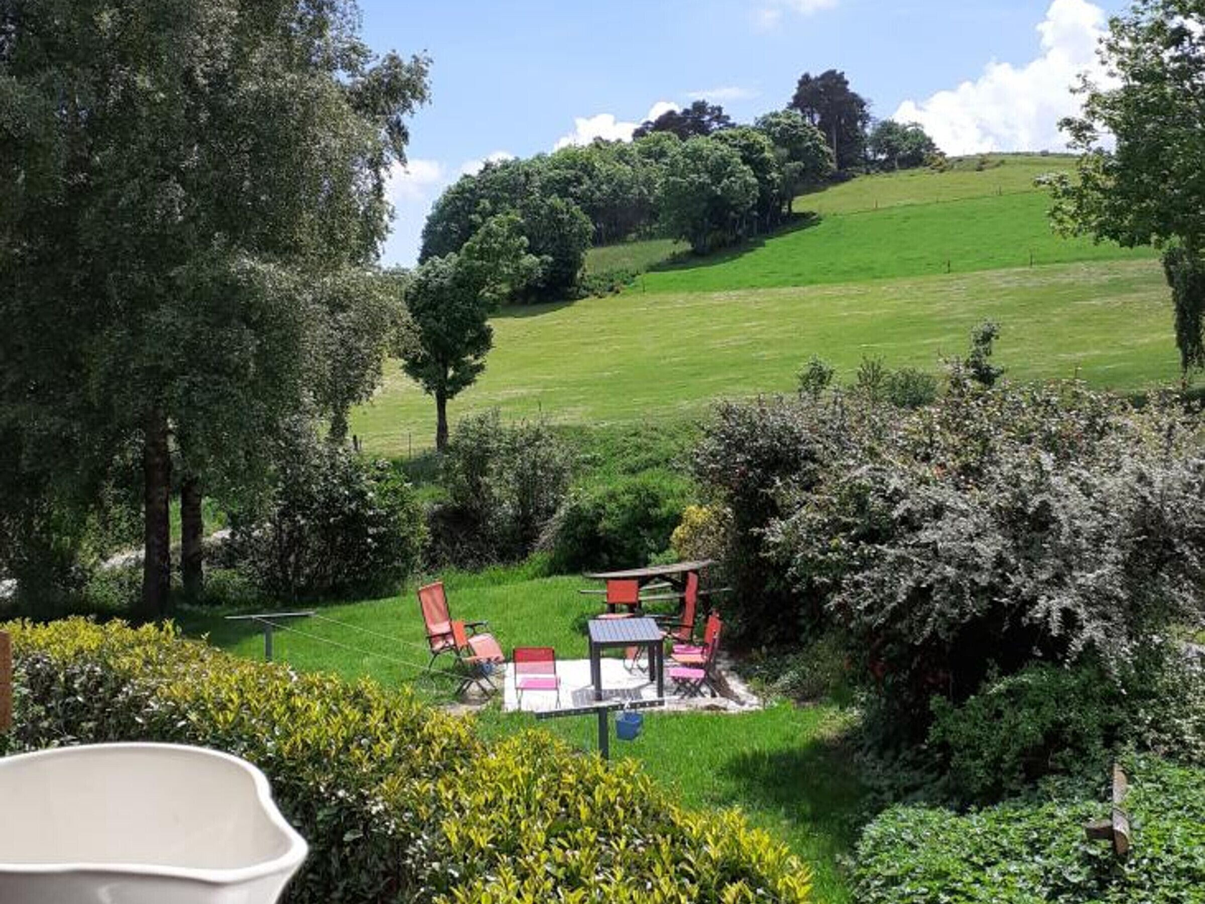 Un jardín con zona de comedor, que incluye una mesa y sillas, rodeado de abundante follaje y árboles.