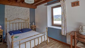 Un dormitorio con techo de madera, una cama con estructura metálica, una ventana con vistas al exterior y un pequeño armario de madera.