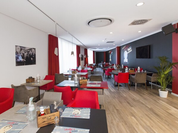 A modern restaurant with red and grey chairs, wooden tables, and a potted plant.