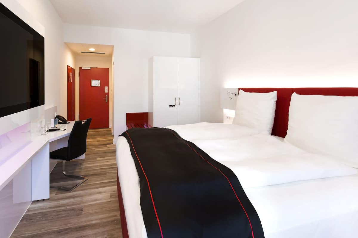 A modern hotel room with a large bed, a desk, and a wardrobe.