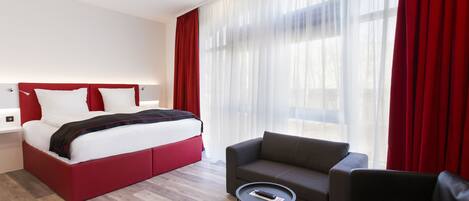 A modern hotel room with a large bed, a sofa, and a small table.