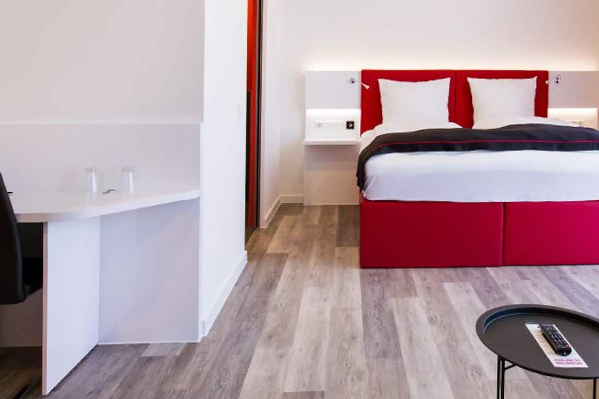 A hotel room with a bed, a desk, a chair, a sofa, and a small table.