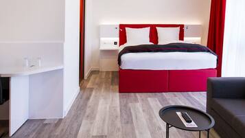 A hotel room with a bed, a desk, a chair, a sofa, and a small table.