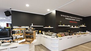 Un desayuno buffet moderno con una variedad de alimentos y bebidas, muebles blancos y una pared de acento negra con una cita inspiradora.