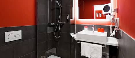 Un baño moderno con ducha envuelta en vidrio, un lavabo blanco y un espejo grande.