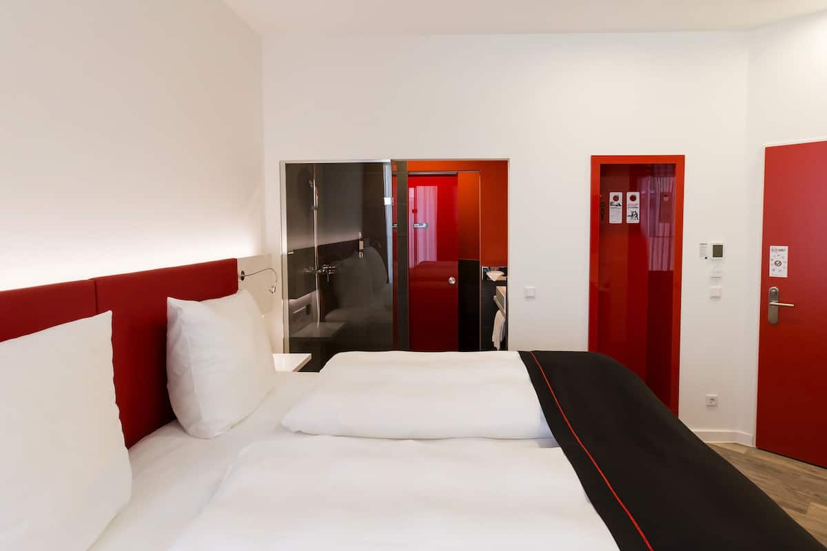 A hotel room with a large bed, a shower area, and red doors.