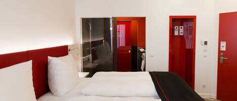 Habitación de hotel con una cama grande, zona de ducha y puertas rojas.