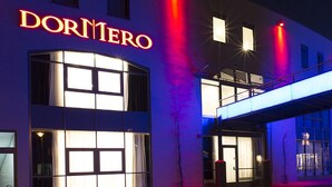 Un edificio con un llamativo letrero de 'DORMERO', un vestíbulo cubierto y una calle con vehículos en movimiento.