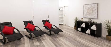 Una habitación con tres sillas negras con cojines rojos, un aparador negro con objetos decorativos y una planta en maceta.
