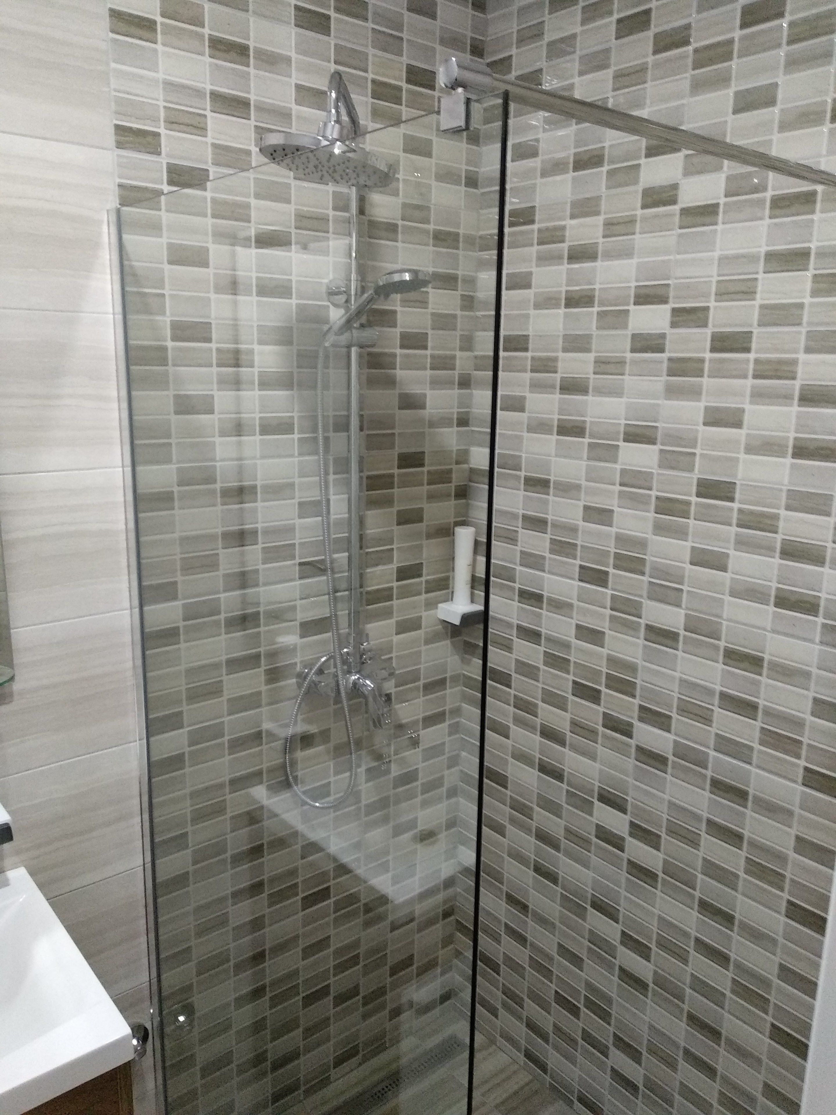 Una ducha con cerramiento de vidrio y pared de azulejos.