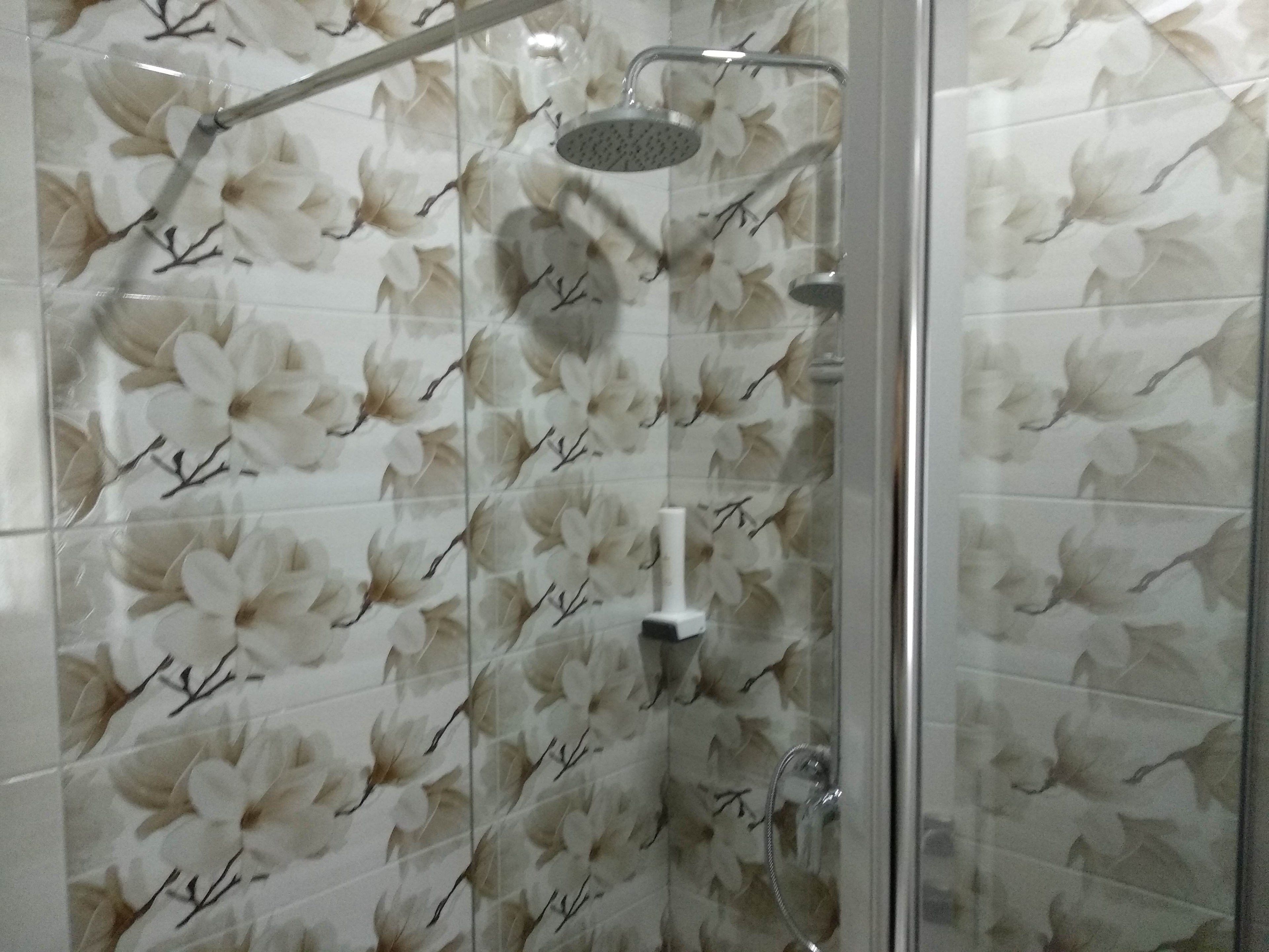 A shower with a floral tile pattern and a handheld showerhead.