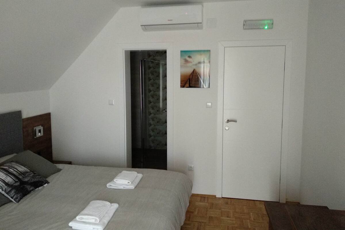 A hotel room with a bed, two towels, a door with a picture, and an air conditioning unit.