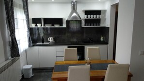 A modern kitchen with white cabinets, a black countertop, and a stainless steel range hood. There is a dining table with four chairs and a vase of flowers on the table.