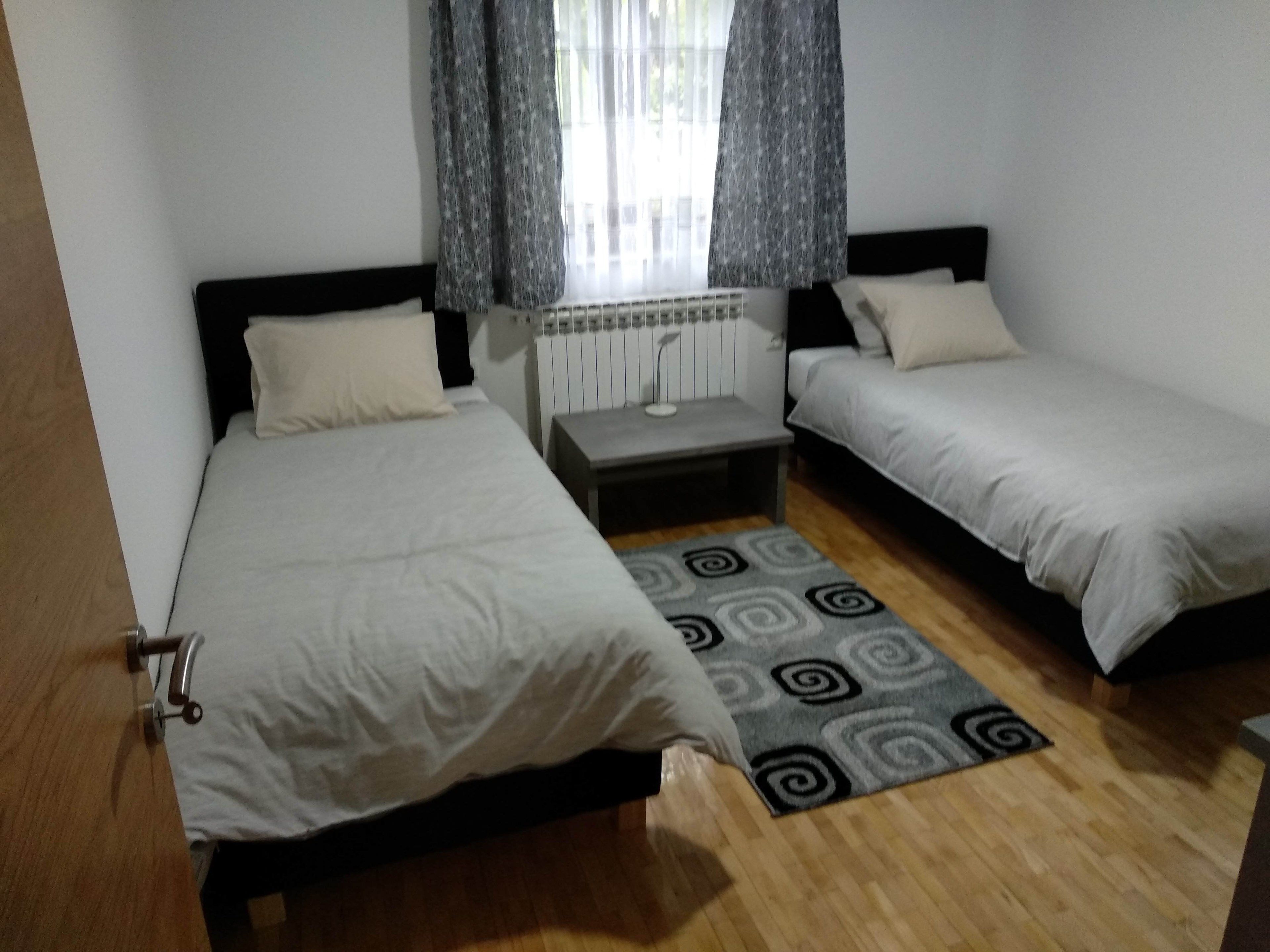 Habitación con dos camas, un radiador, una mesita pequeña y una alfombra estampada.
