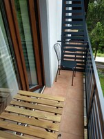 Un balcón con un banco de madera, una silla de metal y una barandilla metálica.