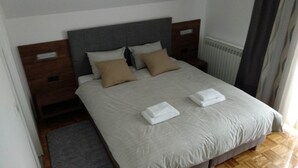 A neatly made bed with white linens and two folded towels, a grey headboard, and a grey rug beside the bed.