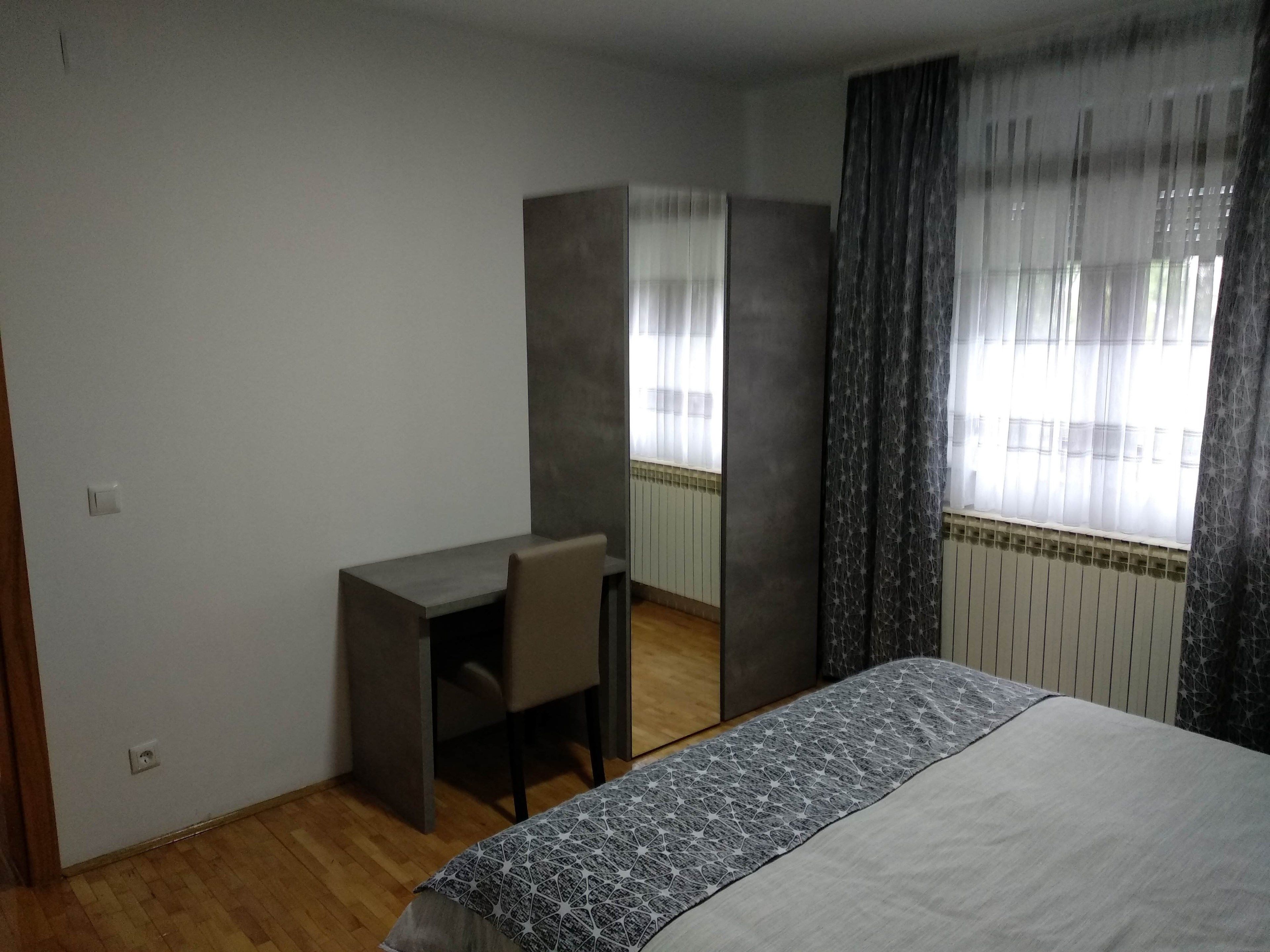 A bedroom with a bed, a desk, and a chair. There is a window with curtains.