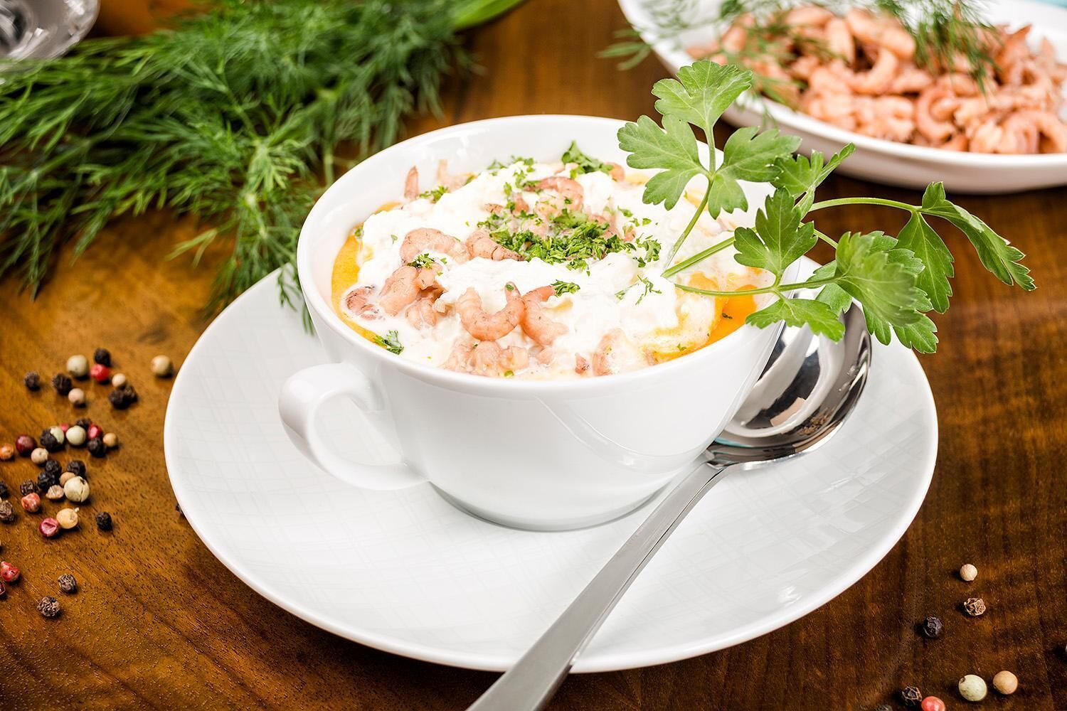 Eine weiße Schüssel Suppe mit Garnelen und Petersilie auf einem Holztisch.
