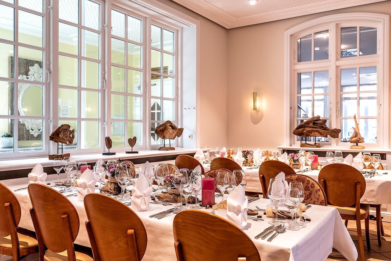 A dining area with multiple tables set for a meal, large windows with decorative items, and a warm interior design.