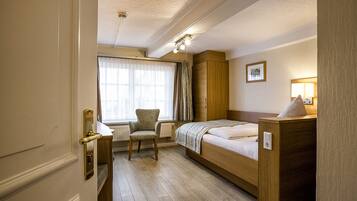 Ein Hotelzimmer mit Bett, Stuhl, Schreibtisch und einem fenster mit Vorhängen.
