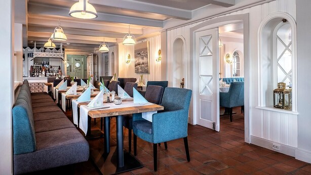 En restaurang med långa, gemensamma bord, blå klädda stolar och en bardisk i bakgrunden.