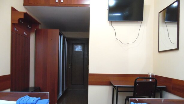 Ein Hotelzimmer mit zwei Betten, einem Schreibtisch, einem Sessel, einem an der Wand befestigten Fernseher und einem Kleiderschrank.