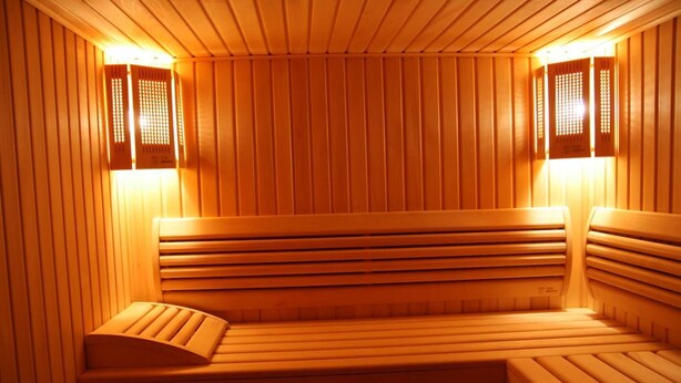 Sauna, jossa on puiset penkit ja säleikköseinät, ja jossa on lämmin valaistus.