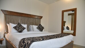 A large bed with a wooden headboard, white bedding, and patterned throw pillows. - Hotel Placid (Prayagraj)