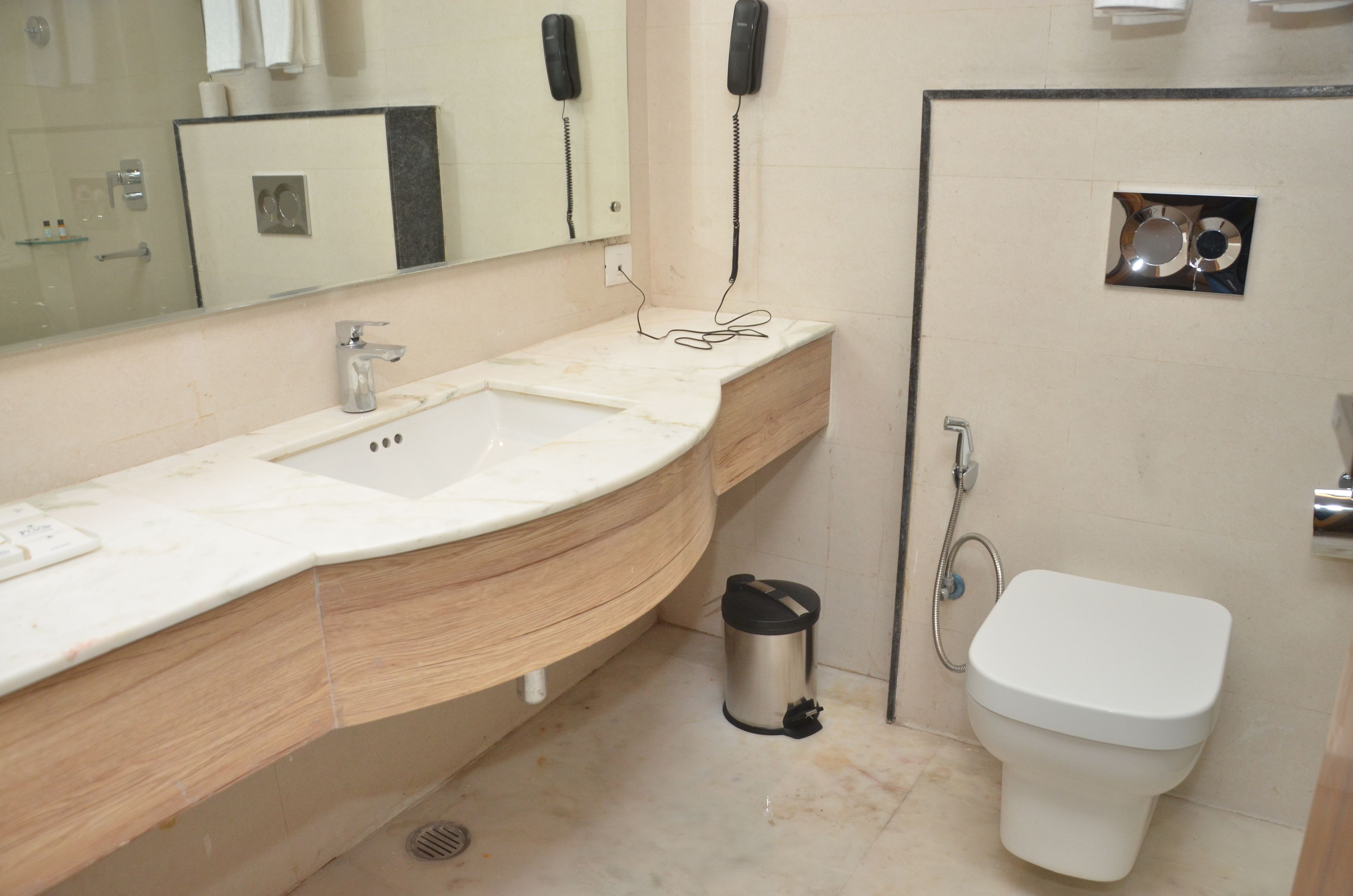A bathroom with a sink, mirror, toilet, and a trash can.
