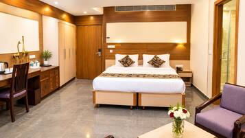A hotel room with a bed, desk, chair, and a small table with a vase of flowers.