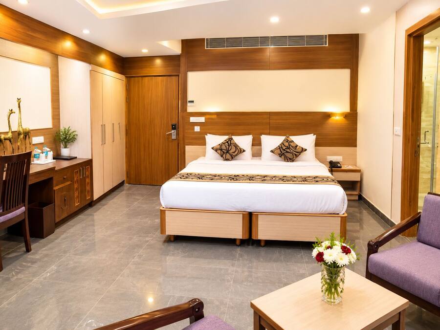 A hotel room with a bed, desk, chair, and a small table with a vase of flowers.