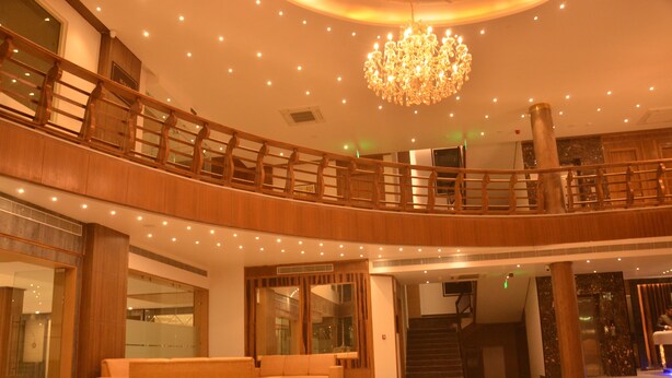 A spacious lobby with a high ceiling, a chandelier, a wooden balcony, and a reception desk. - Hotel Placid (Prayagraj)