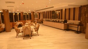 A dining area with wicker chairs and tables, a buffet counter, and a view of the city at night. - Hotel Placid (Prayagraj)
