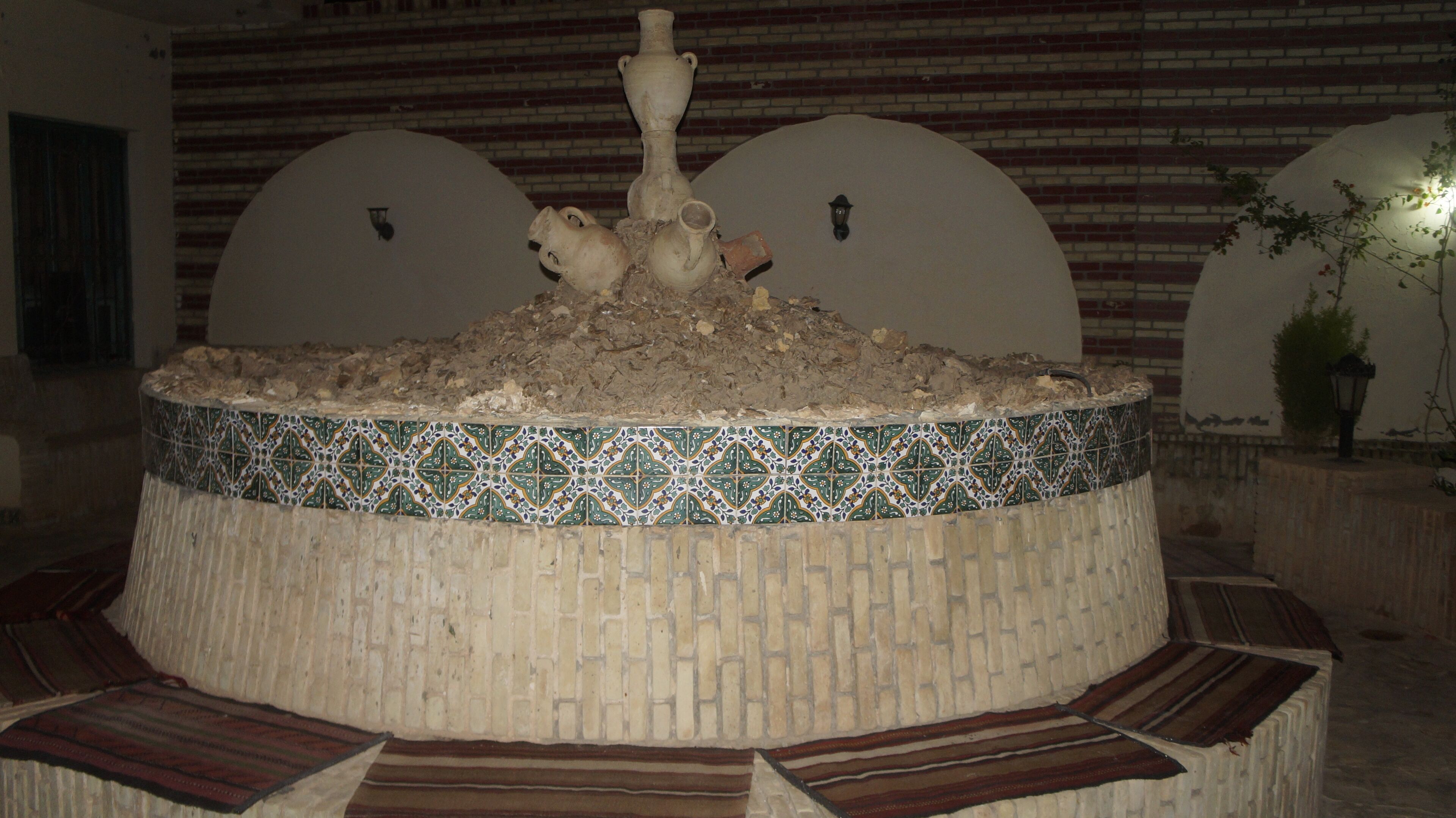 A circular fountain with a mosaic border, set against a brick wall with arched niches.