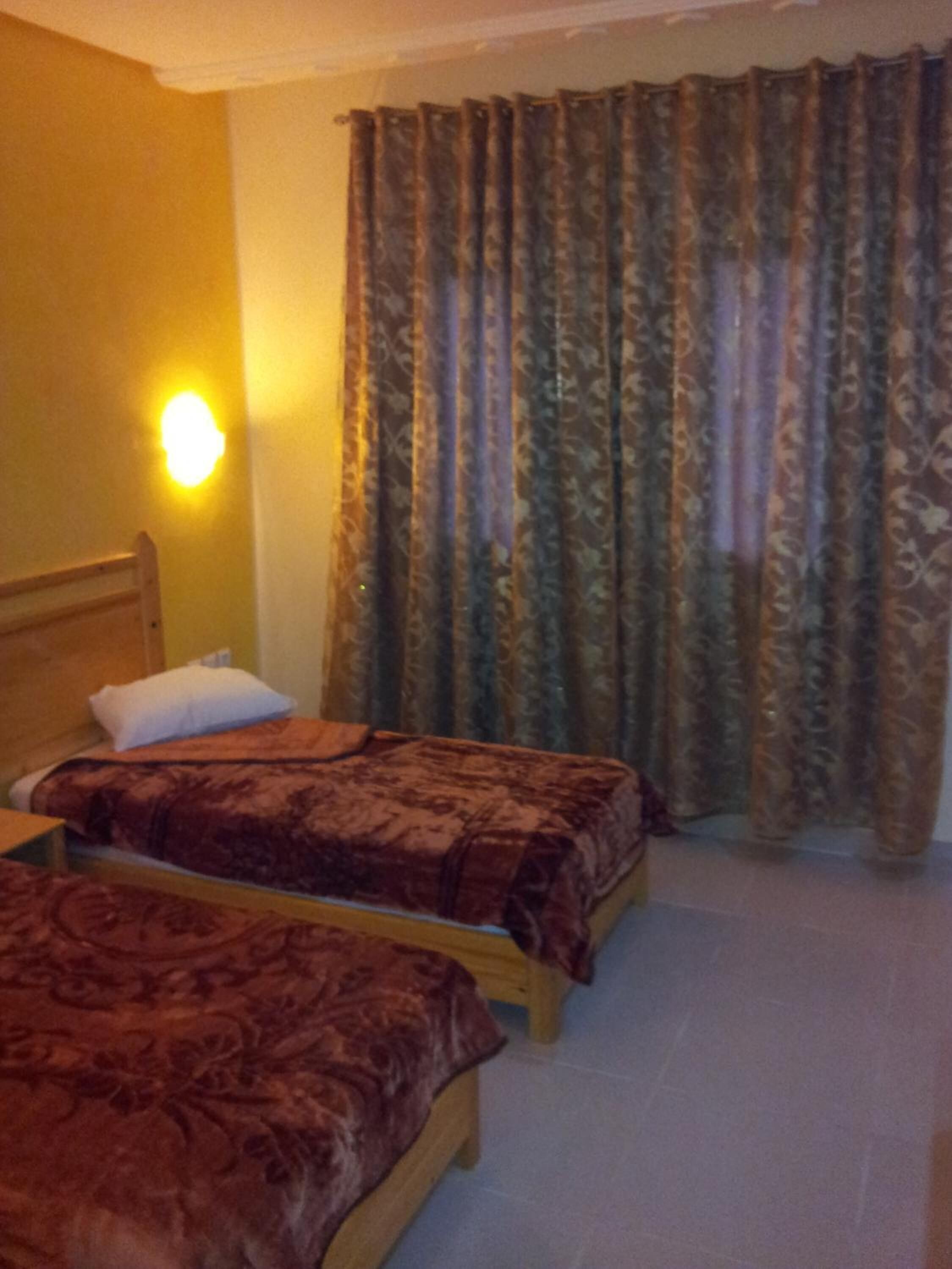 A hotel room with two single beds, a wooden headboard, a night light, and patterned curtains.