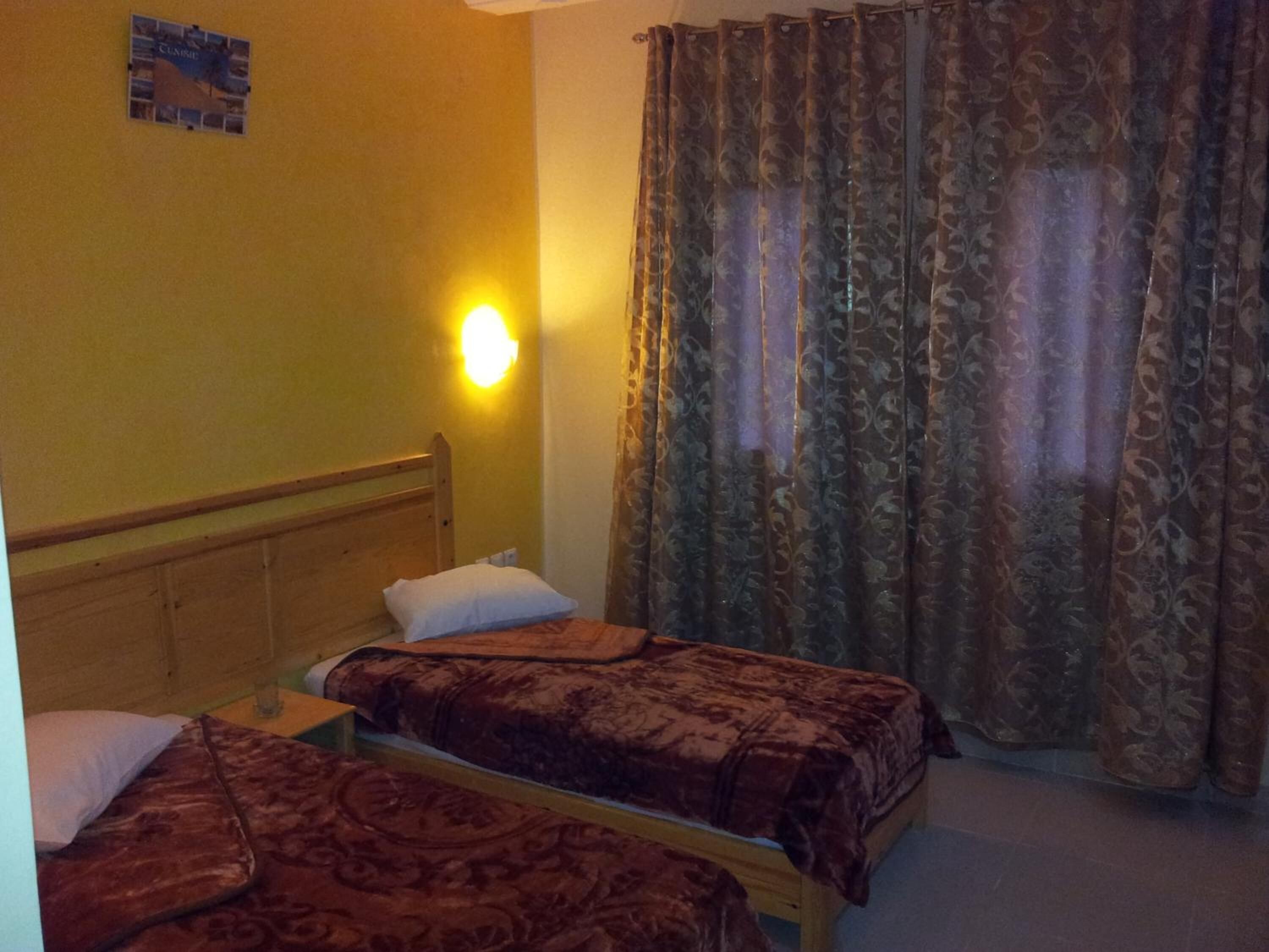 A room with two beds, a wooden headboard, a wall-mounted light, and patterned curtains.